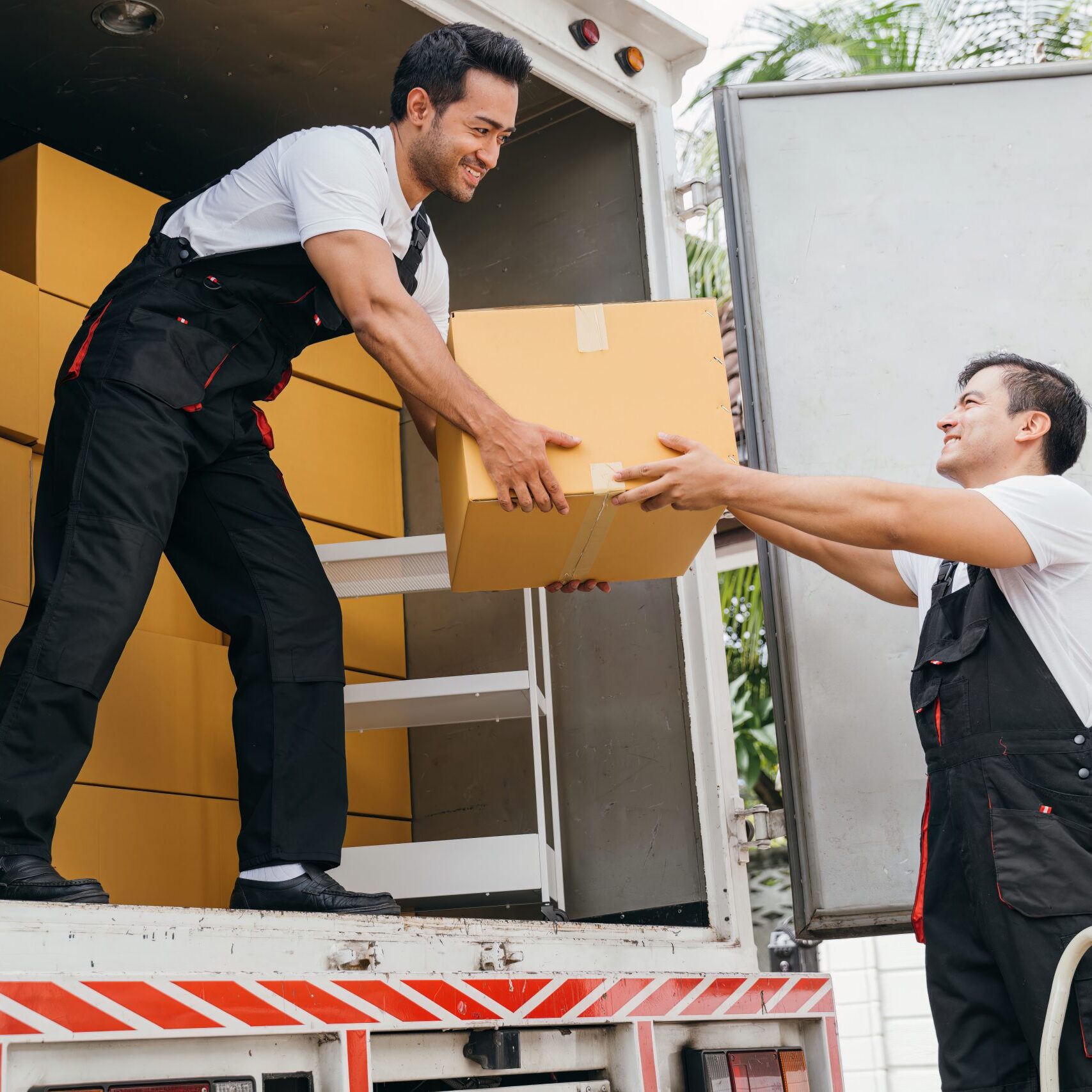 Smiling employees of a removal company work in uniform unloading boxes and furniture from the truck. Their dedication guarantees a smooth delivery into the new home ensuring happiness. Moving Day Smiling employees of a removal company work in uniform unloading boxes and furniture from the truck. Their dedication guarantees a smooth delivery into the new home ensuring happiness. Moving Day